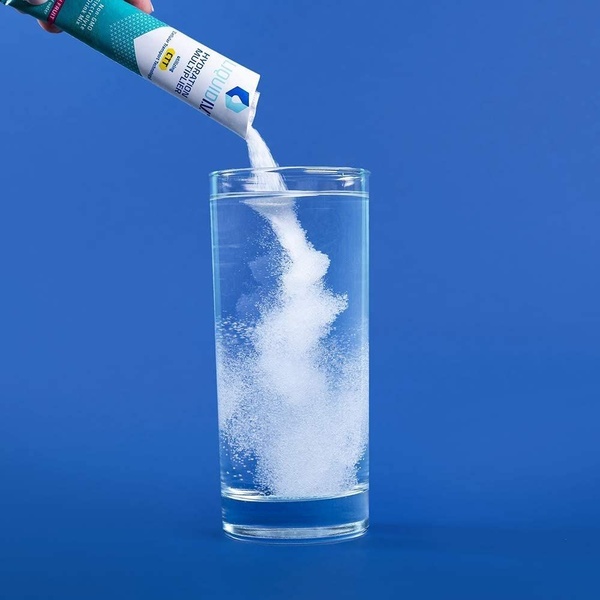A close-up shot of an electrolyte drink mix packet being poured into a clear glass of water against a bold blue background.